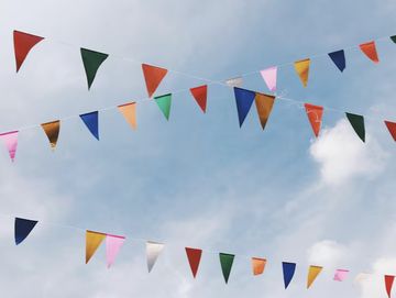 Colorful triangular flags strung across a clear blue sky with scattered clouds.