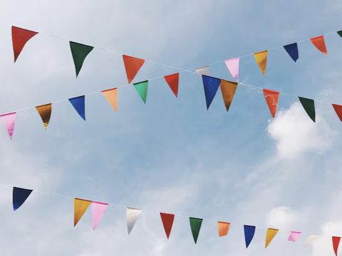 Colorful triangular flags strung across a clear blue sky with scattered clouds.