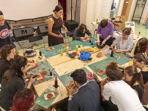 A group of people gathered around tables engaging in an art or craft workshop, with materials and tools spread out in front of them.