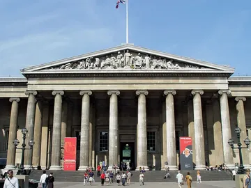 Front view of the British Museum's entrance with neoclassical columns, decorative friezes, and visitors walking on a sunny day.
