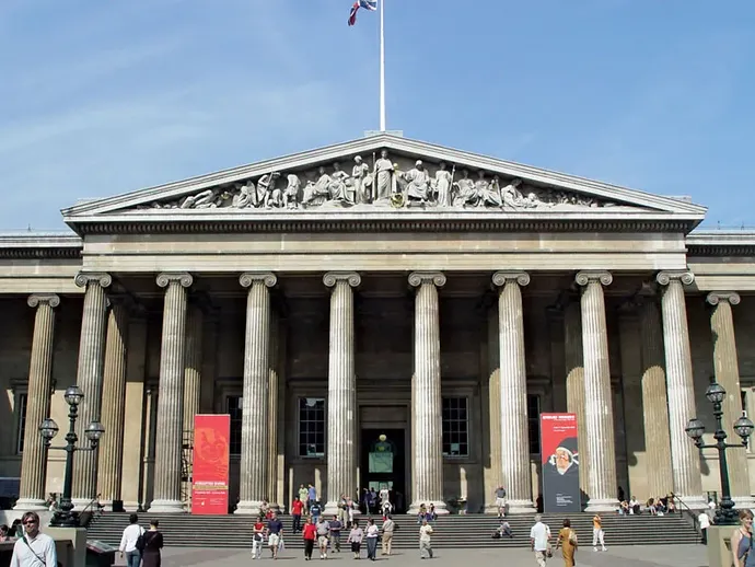 Front view of the British Museum's entrance with neoclassical columns, decorative friezes, and visitors walking on a sunny day.