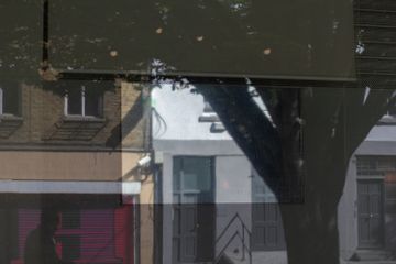 Reflection through window showing street buildings tree, layered glass, muted colors, urban scene soft lightingProvide your feedback on BizChat