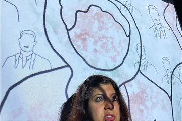 A person stands in front of a large projected illustration featuring outlined figures and abstract shapes.