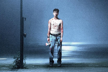 A person stands alone on a dimly lit street at night, covered in red stains and holding an axe at their side.