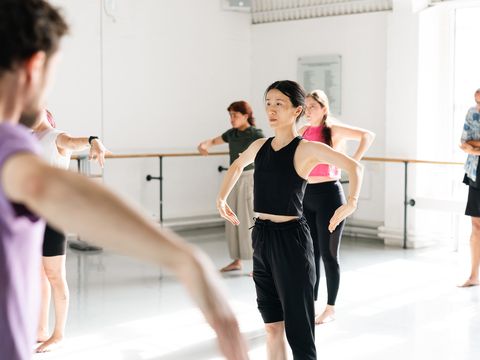 A group of people in casual fitness attire participate in a dance or movement class in a bright studio.
