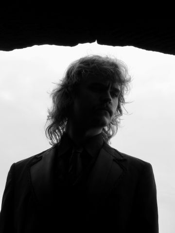 Black and white photo of person with shoulder-length hair, face obscured by shadow