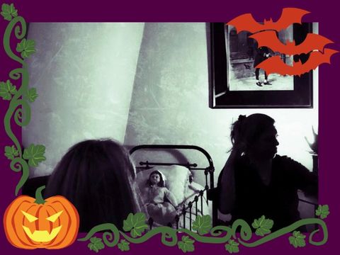 Person in silhouette gestures near a vintage bed with a doll, beside another seated person, with Halloween decorations framing the scene.