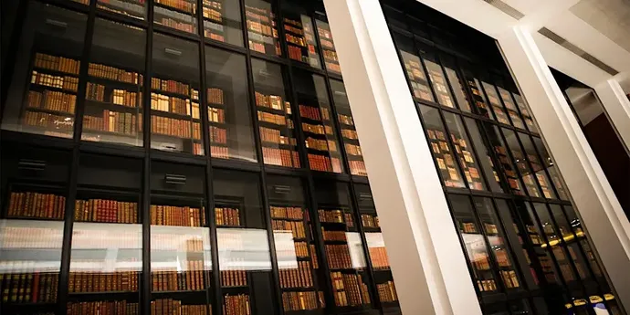 Tall glass bookshelves filled with rows of books in a modern library setting, viewed from a low angle.
