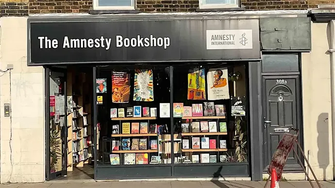 Front view of The Amnesty Bookshop with large glass windows displaying books and posters, and a black sign above reading 'The Amnesty Bookshop' alongside the Amnesty International logo