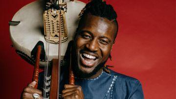 Smiling person holding a traditional string instrument against a red background.