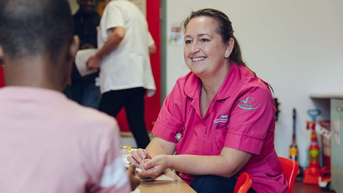 A female nursing assistant dressed in pink in consultation with a patient