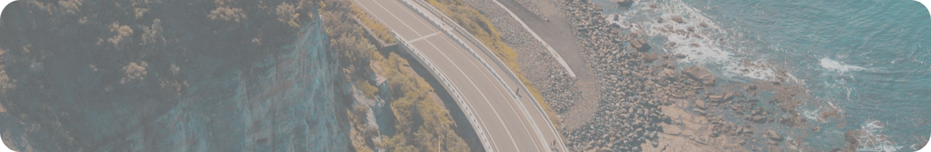 A road runs between a steep cliff on the left and the sea on the right.