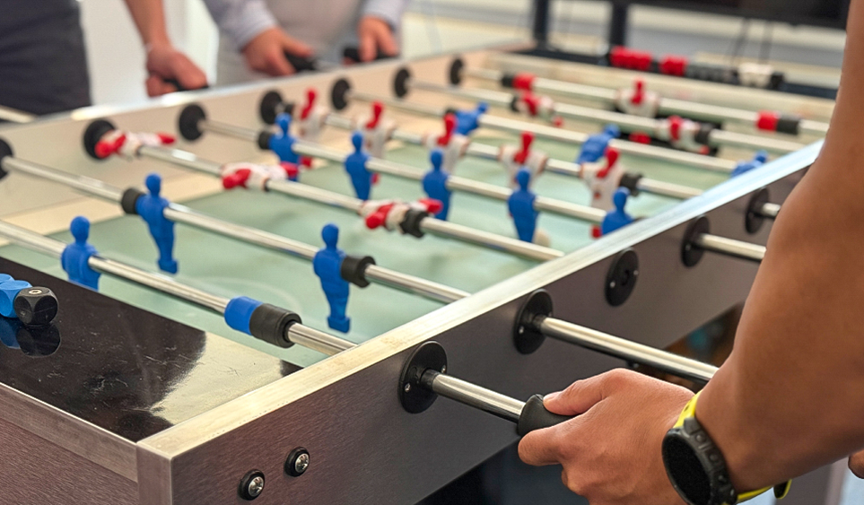 Mitarbeitende spielen Kicker im Büro.