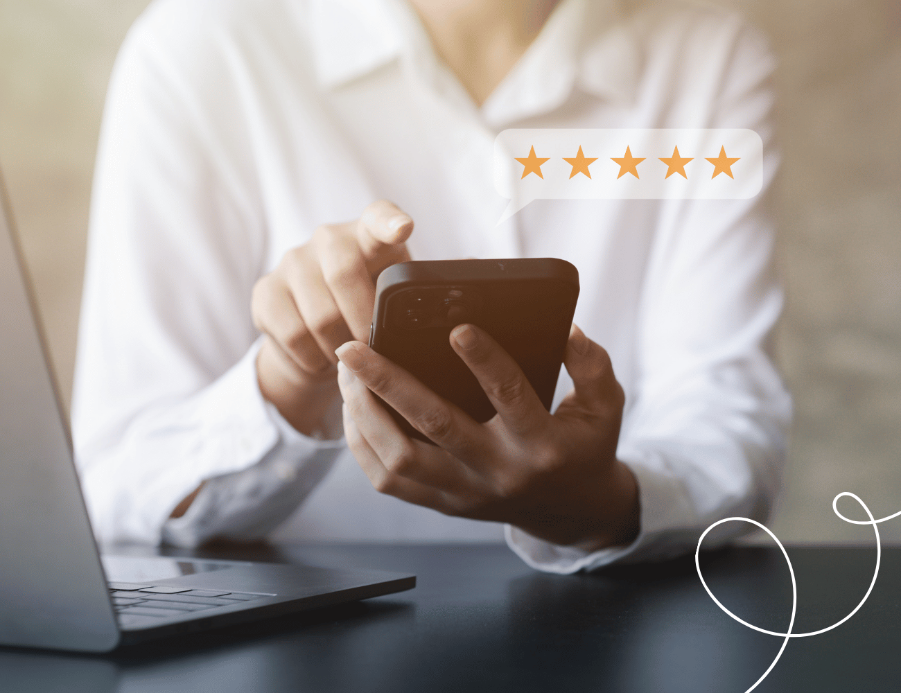 Person in einem weißen Hemd, die ein Telefon hält und auf den Bildschirm tippt. Darüber befindet sich eine Sprechblase mit fünf Sternen. Auf dem Tisch steht ein Laptop.