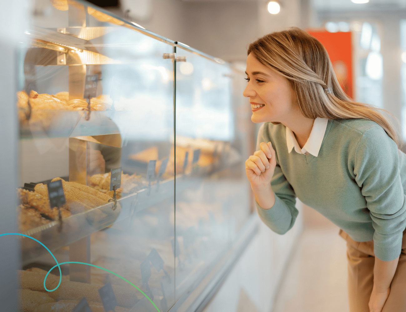 Lächelnde junge Frau, die sich zu einer Bäckereitheke beugt und die Backwaren hinter dem Glas bewundert.