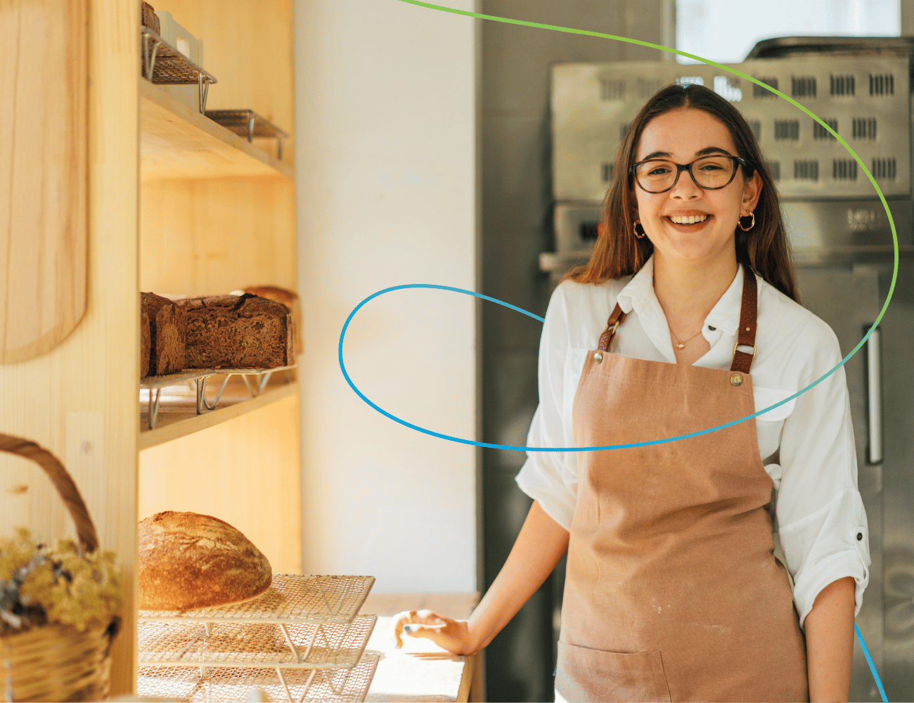 Eine lächelnde junge Bäckerin mit Brille und brauner Schürze steht neben Holzregalen mit Broten in einer gemütlichen Bäckerei.