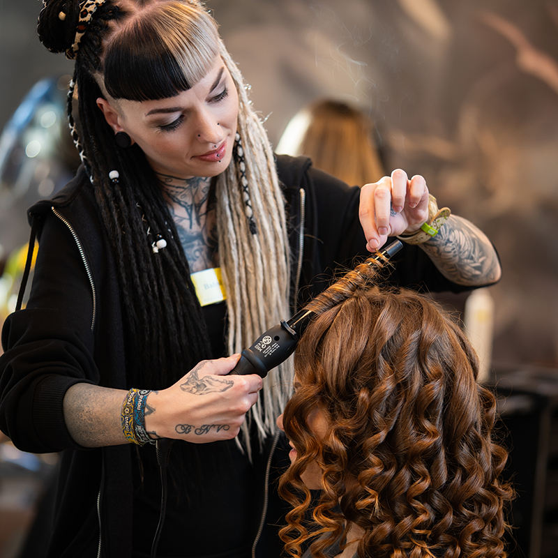 Friseurin stylt das braune Haar einer Kundin mit einem Lockenstab.