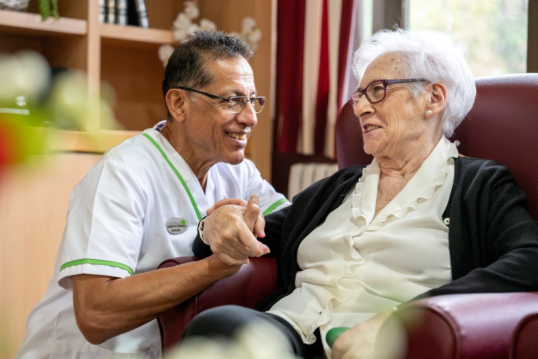 Aide soignant accroupi à côté d'une résidente souriante à l'ehpad rivalières