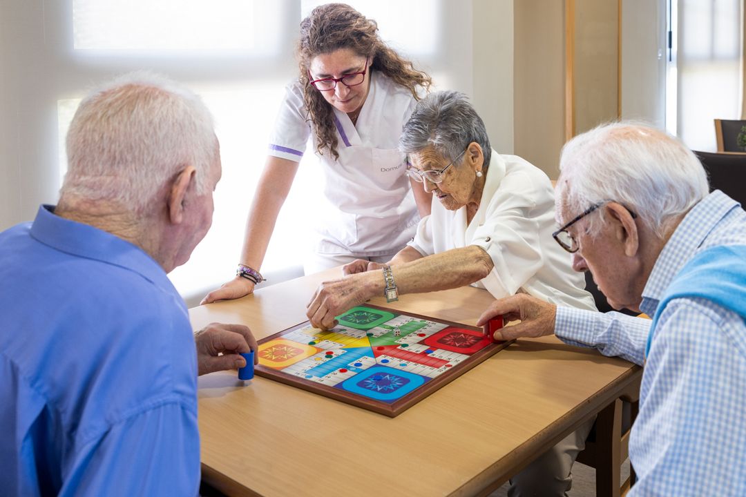 Cuidadora y personas mayores jugando al dominó