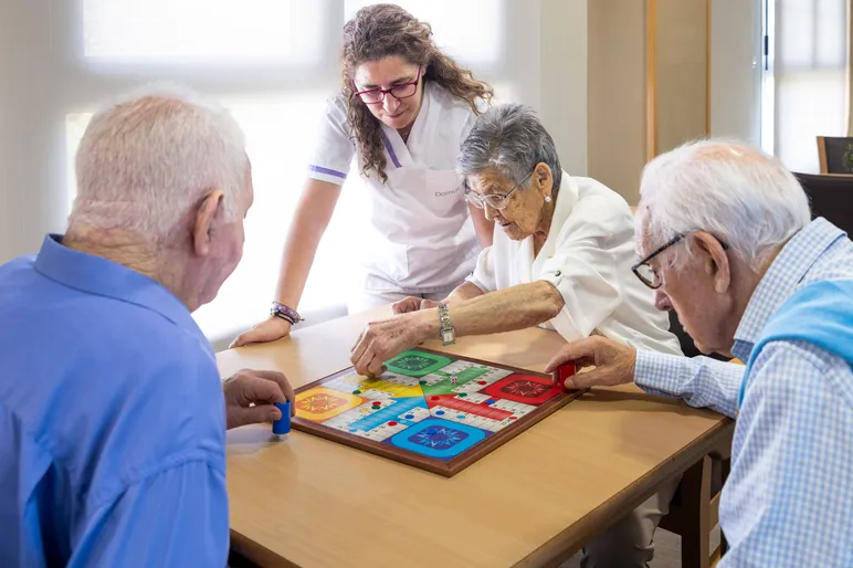 Mayores y cuidadora jugando al parchis