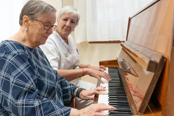 persona mayor y cuidadora tocando el piano