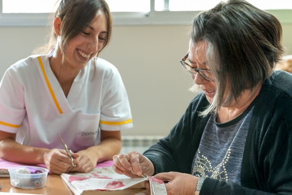 persona mayor y cuidadora remendando una tela