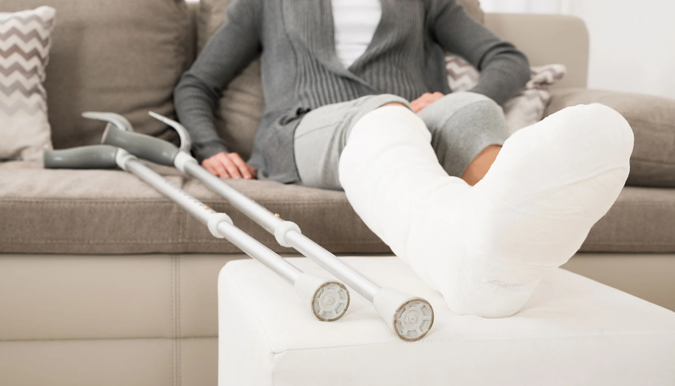 une personne assise avec une jambe dans le plâtre posée sur un pouf