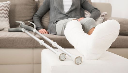 une personne assise avec une jambe dans le plâtre posée sur un pouf