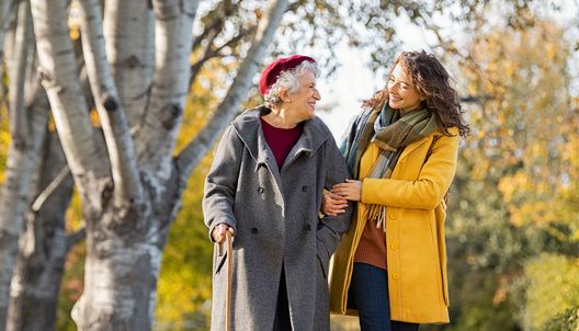 une femme âgées se promène dans un parc avec une auxiliaire de vie