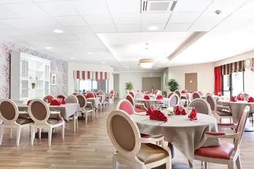 Salle commune de restaurant Les Jardins de Saintonge avec tables et cahises blanc marron, lumineuse avec rideaux rouges à rayures