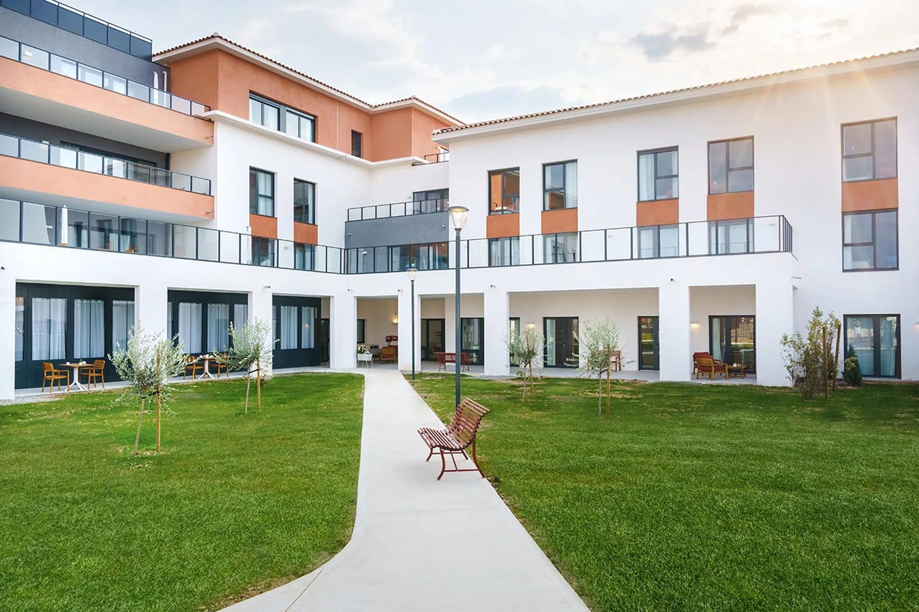 Façade batiment moderne neuf pelouse, beaucoup de fentres et balcons terrasses, forme cubique blanc gris orange