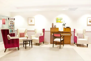 Salon avec piano bois vintage, belle éclairage et fauteils blanc et bordeaux velour, mur blanc avec tableaux