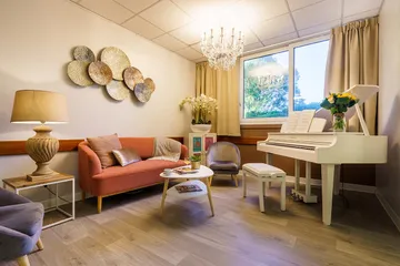 Salon détente vue jardin décoration beige et blanc avec canapé rouge et coussins, grand piano blanc à queue et lustre