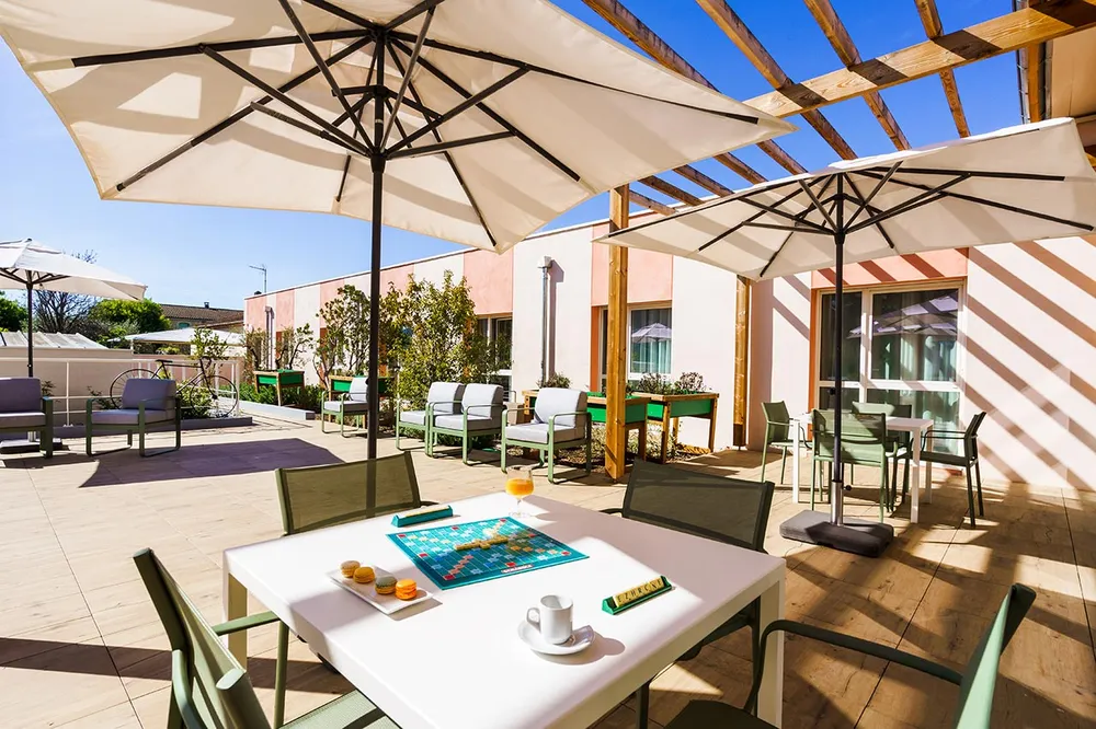 Terrasse et cour intérieure maison retraite Les Sereins à Cheval-Blanc moderne villa soleil avec parasol beige et tables et chaises