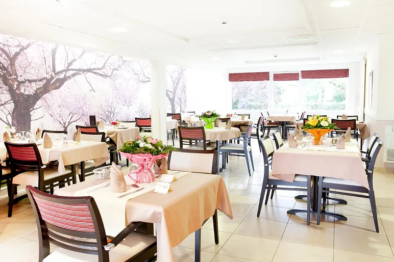 Salle de restaurant avec tables carrées dressées avec bouquet fleurs frais, mur sakura japonais et lumière naturel fenêtre exposition sud