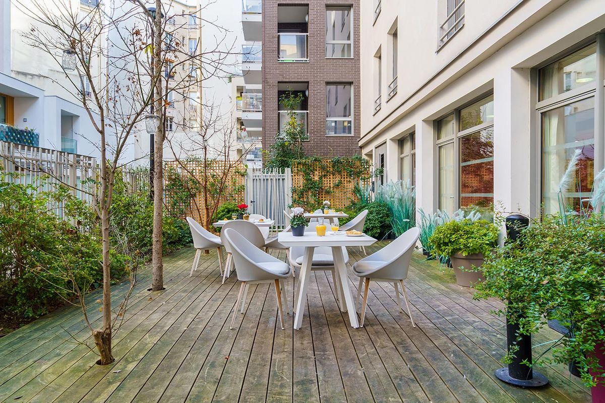 Balcon cours intérieure lumineux chaleureux avec végétation et tables Résidence Ornano à Paris