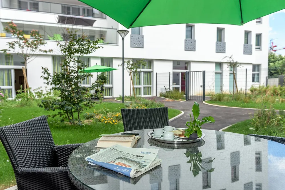 Vue cour intérieur facade Résidence Les Intemporelles Aubervilliers jardin chaise et table en verre parasol