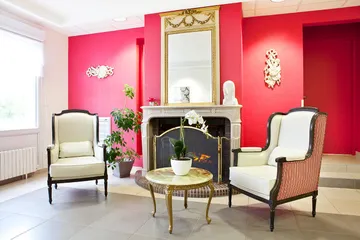 Cheminée vintage bourgeois france mur rouge avec grand mirroir dorée et fauteils vintage blanc velour, table basse ronde marbre orchidée