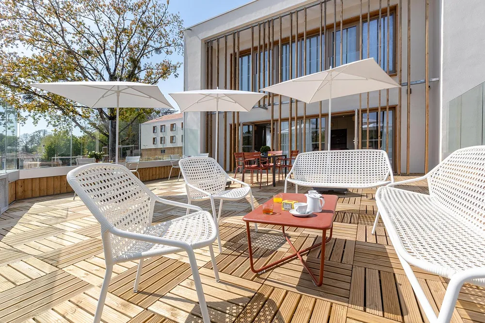 Terrasse balcon moderne et chic avec sol en bois, parasol blanc et salon de jardin avec facade immeuble en fond