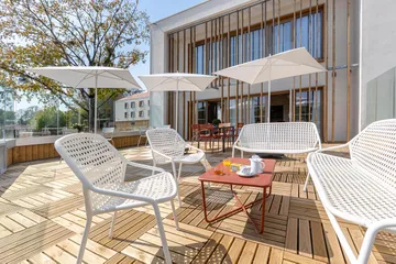 Terrasse balcon moderne et chic avec sol en bois, parasol blanc et salon de jardin avec facade immeuble en fond