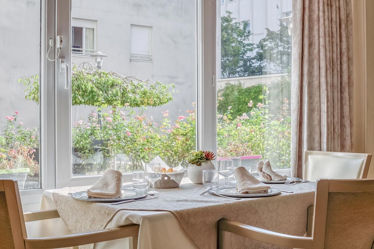 Table à manger près d'une fenêtre donnant sur un jardin maison de retraite à Asnières