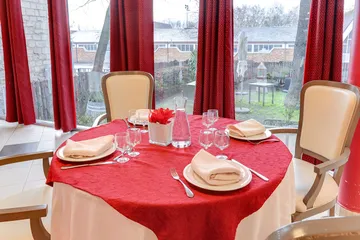 Vue sur table ronde rouge décorée  maison retraite Médicis à Argenteuil  vue sur jardin baie vitrée rideaux rouges