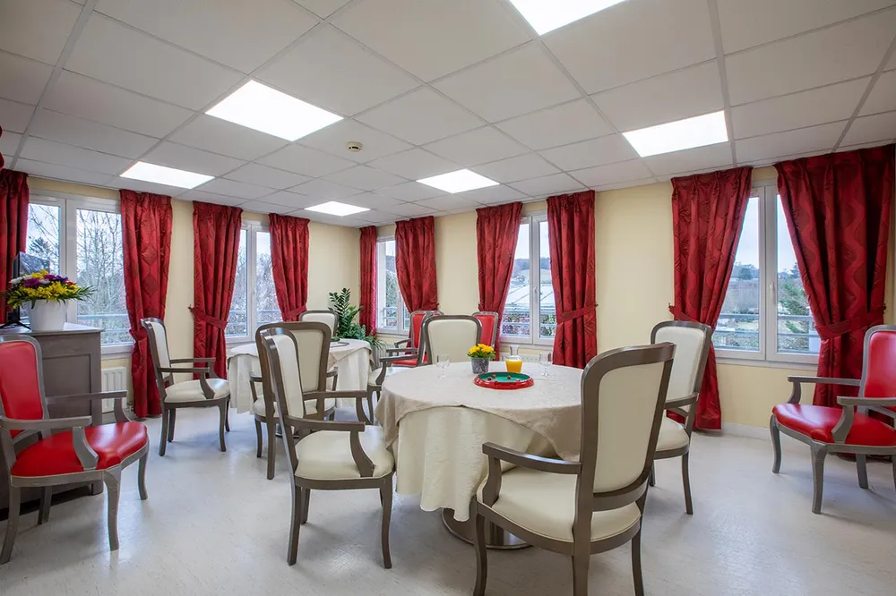 Salle de restauration beige et rougfe avec tables rondes en maison de retraite à Trie Château, Les Jardins de la Tour