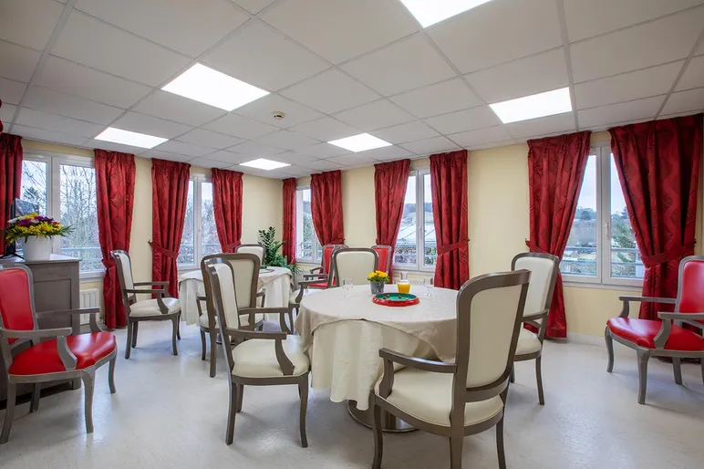 Salle de restauration beige et rougfe avec tables rondes en maison de retraite à Trie Château, Les Jardins de la Tour