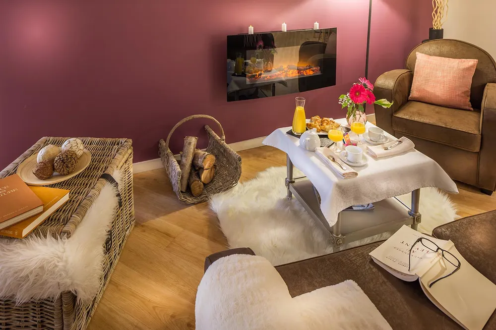 Salon zen et cocooning avec cheminée feu de bois, fauteils brun, mur prune et cozy