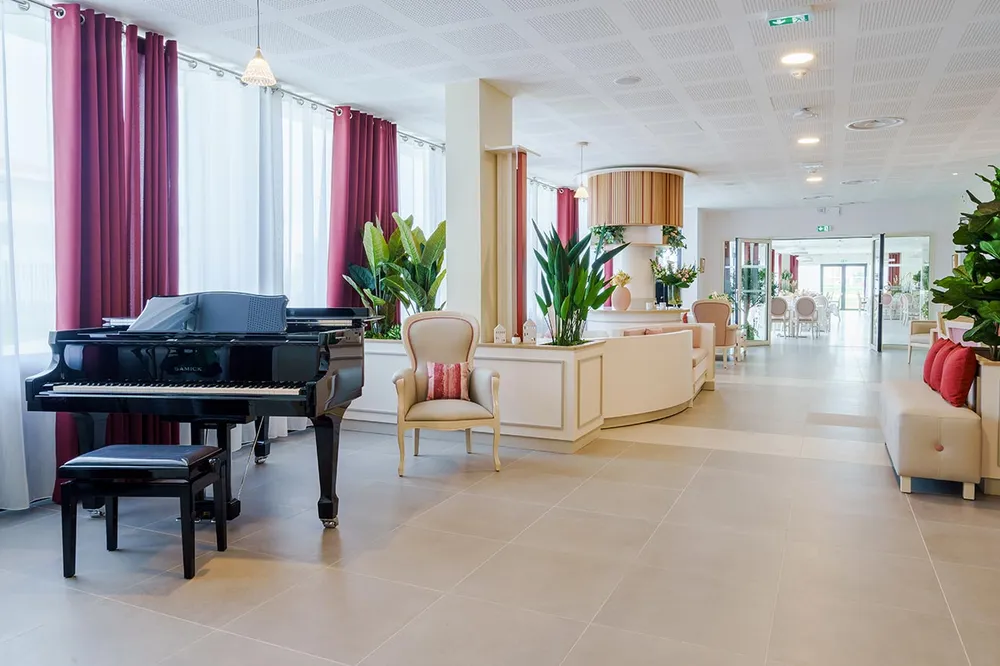 Grande salle réception avec piano à queue noir thème blanc beige et framboise lumineuse architecture luxe hotel chic fauteils beige et coussins roses