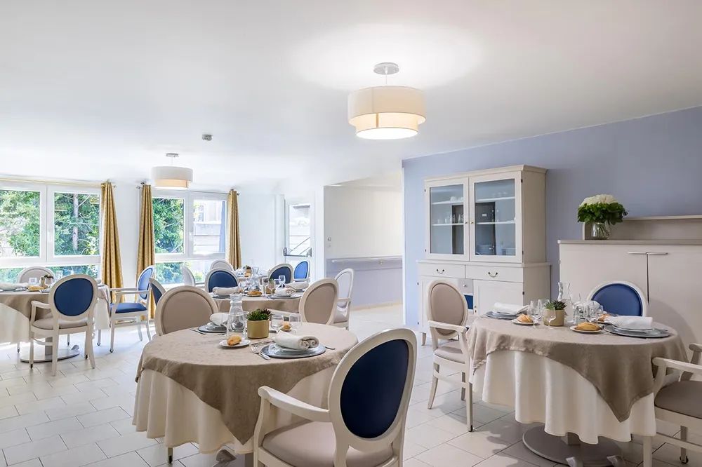 Salle à manger lumineuse avec placards et tables rondes dressées à l'ehpad Azur à Colombes