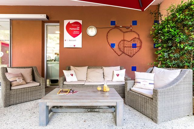Coin détente extérieur avec mobilier en osier, coussins beige et table en bois à La Résidence Palmeraie