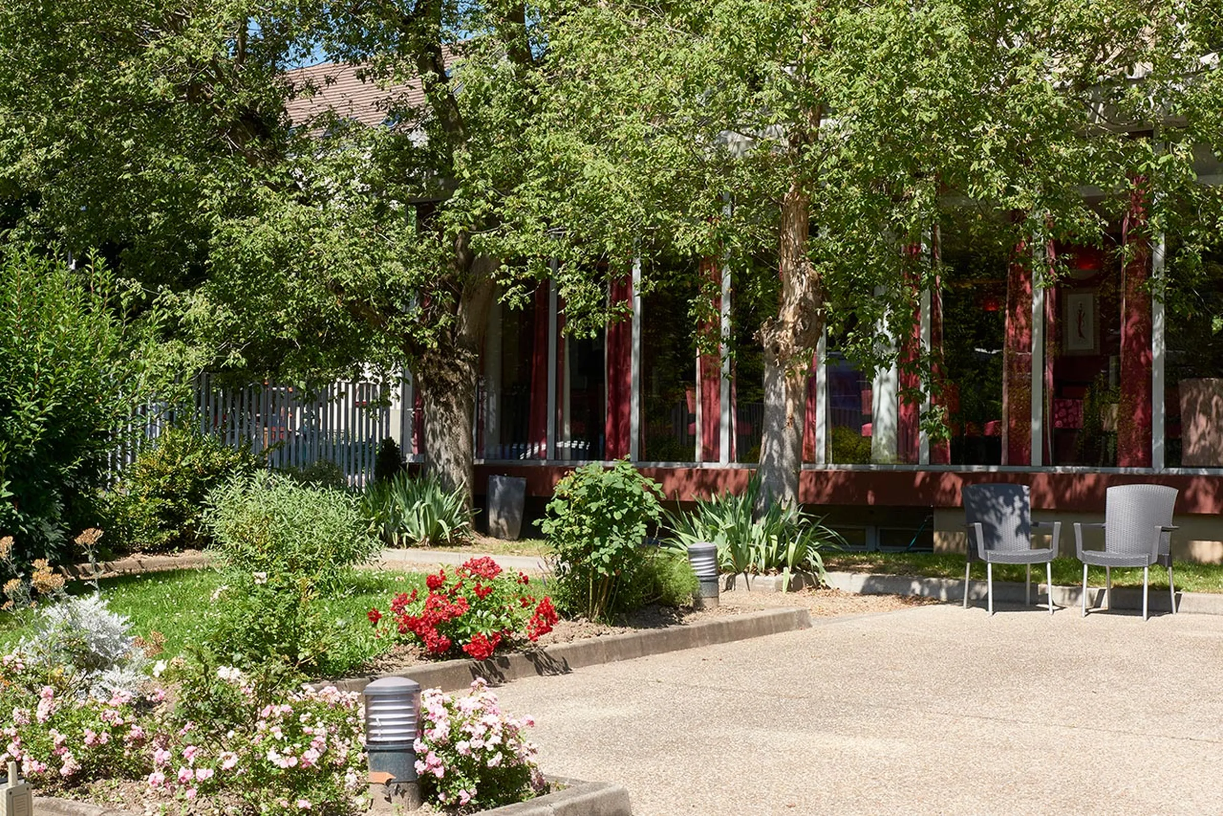Vue jardin fleurs et nature bien entretenu avec chemin gravier et batiment rouge en fond