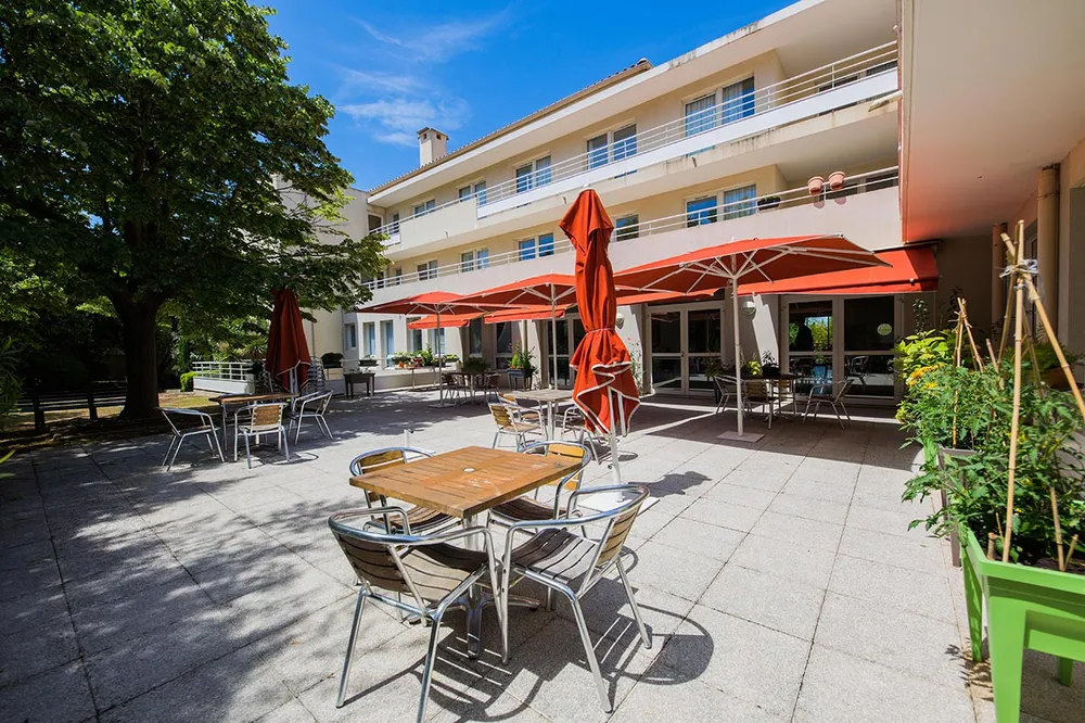 Terrasse avec tables et chaises en bois pour jardin, avec parasols rouges en ehpad à Marseille, Résidence Mazargues